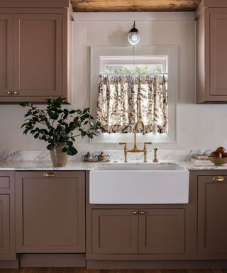 dark pink kitchen with a butler sink and floral cafe curtain at the window