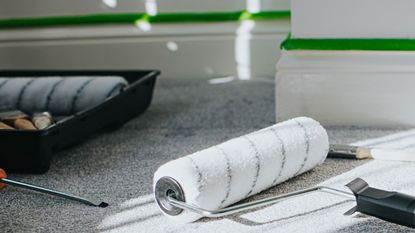 A clean paint roller on the floor in front of a wall with painters tape