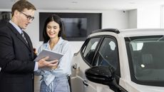 A car salesman talks with a young female customer in a dealership.