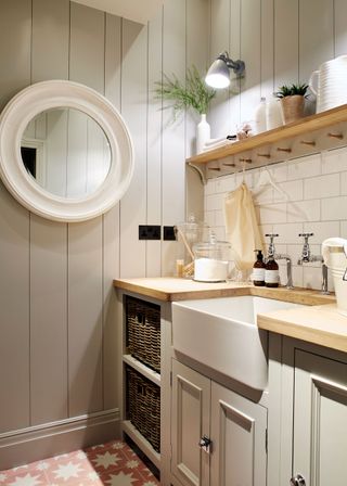 A wood panelled pale gray laundry room scheme with butler sink, white subway tiles and wooden countertops and open shelf.