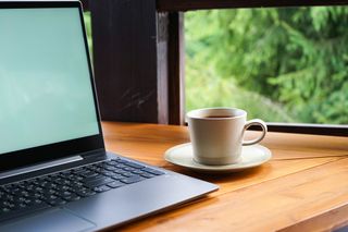 A laptop and a coffee on a wooden table next to a window looking out at a garden