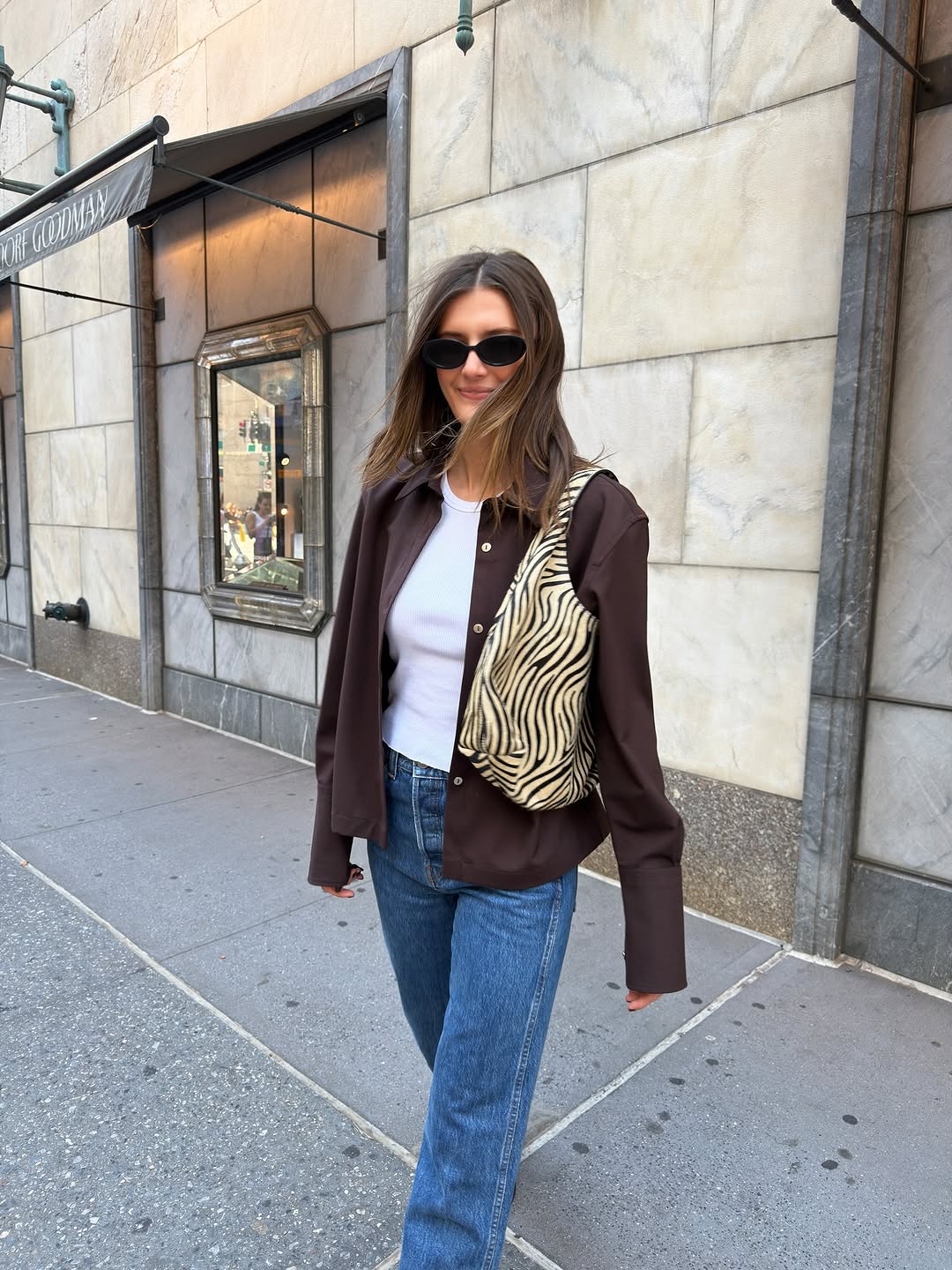 Woman wearing a white tee, jeans, a brown button-down, and a zebra print tote bag.