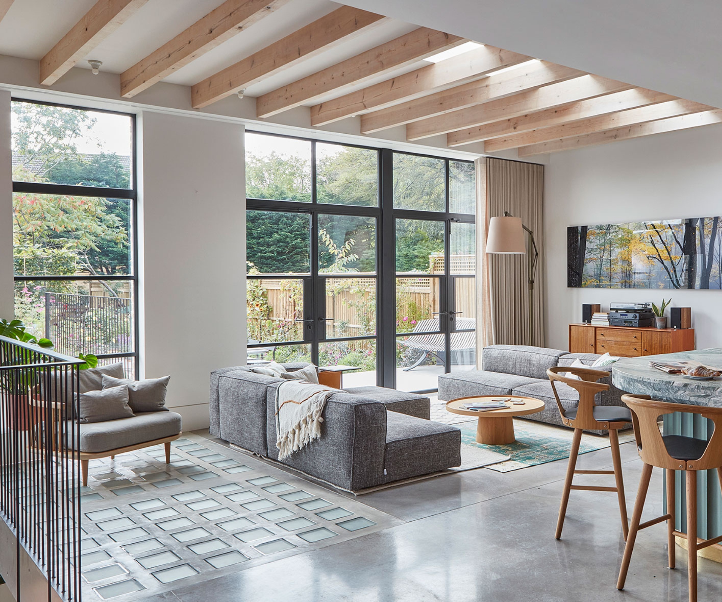 Open-plan kitchen and lounge with marble island, wooden stools, grey sofa, exposed beams, glazed doors to garden.