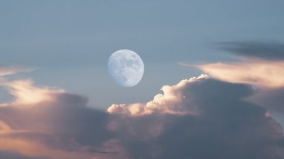 The nearly-full daytime moon hangs dimly in a blue sky near clouds