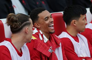 Trent Alexander-Arnold of Liverpool reacts as he speaks to teammate Kostas Tsimikas whilst sat on the substitutes bench prior to the Premier League match between Liverpool FC and Arsenal FC at Anfield on May 11, 2025 in Liverpool, England.