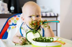 Close up of baby eating green puree messy all over face