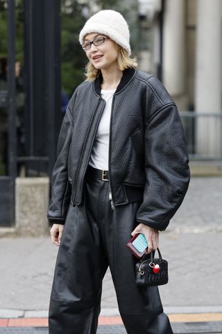 Gigi Hadid wears white top, black leather jacket, black leather pants, black ballet shoes, white beanie, black Miu Miu bag, outside Miu Miu, during the Womenswear Fall/Winter 2025/2026 as part of Paris Fashion Week on March 11, 2025 in Paris, France.