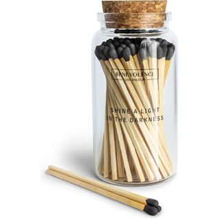 A clear glass jar with wooden matches inside, black tips. A cork lid on the jar