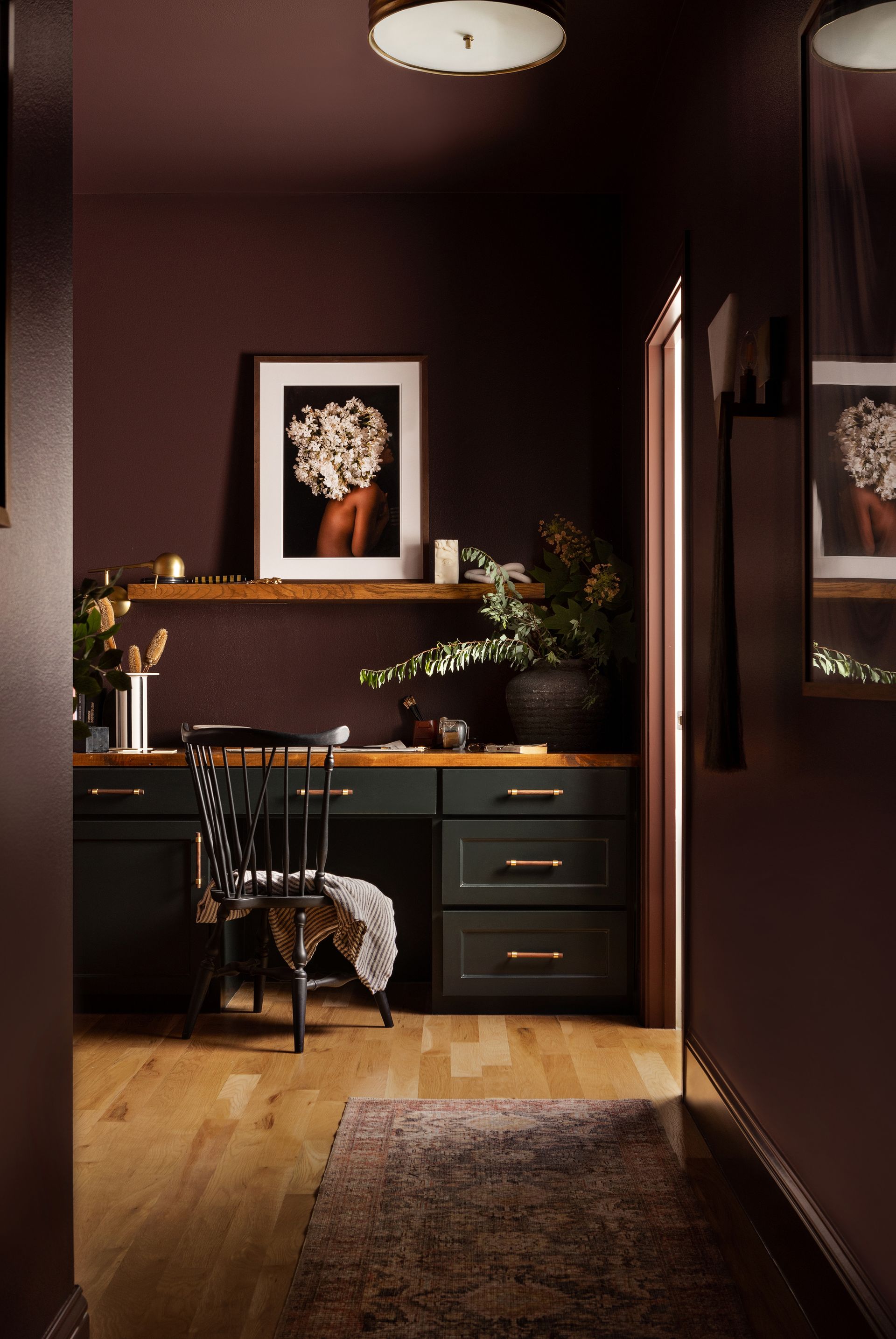 A home office space color drenched in a deep burgundy shade with a desk in an alcove