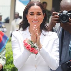 Meghan Markle wearing a white suit in nigeria with a corsage and an aurate necklace