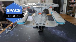 A grey brick-built spaceship stands on a black display stand on a starry mat on a table with minifigures lined up next to it. The Space.com logo is in the top left corner.