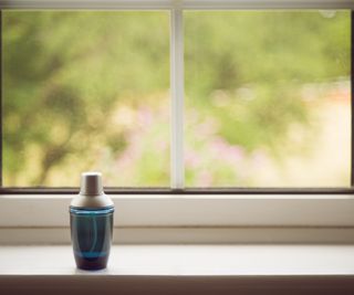 A blue bottle of unknown liquid on a white gloss window sill. The view outside is blurry but suggests greenery or foliage