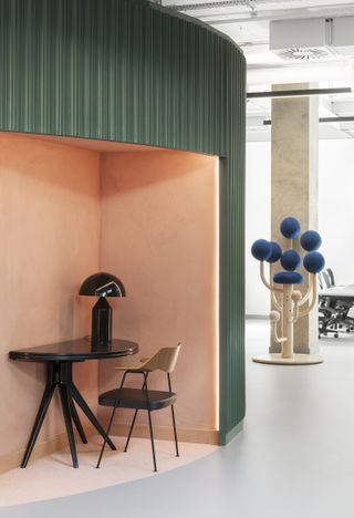 A blue and pink office interior against the wall. A black half-table with lamp and wood chair. A planet-style coat rack and a table and desk located behind.