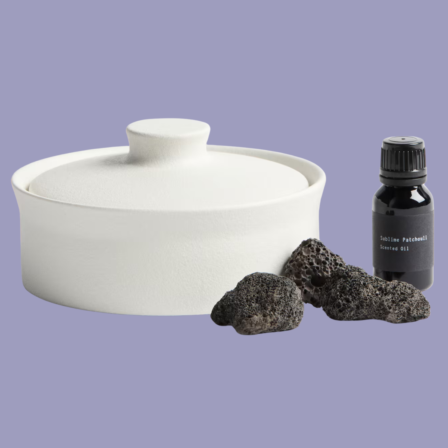 A white vessel with black lava rocks and a bottle of essential oil