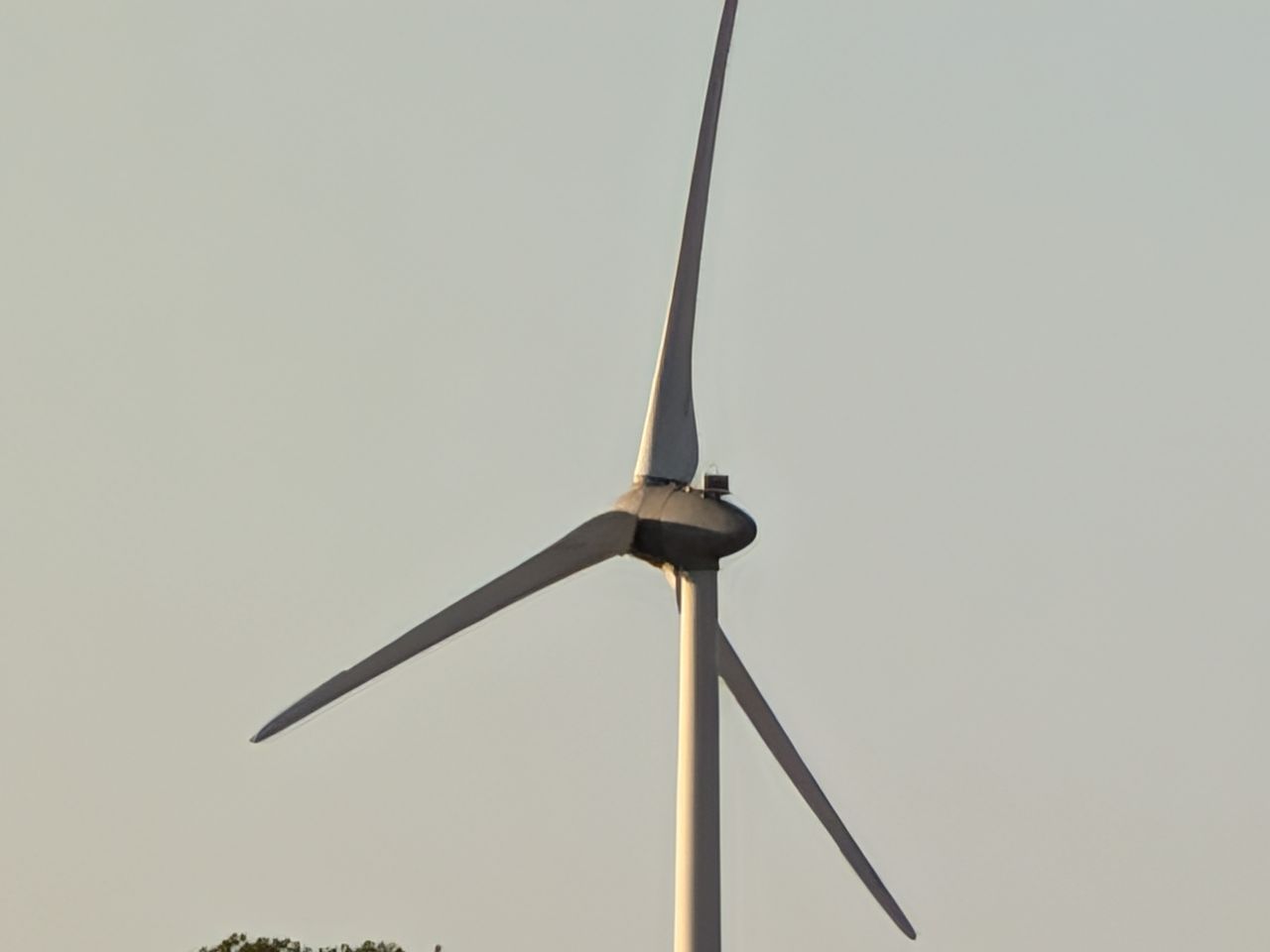 Close-up of a wind turbine against a pale evening sky, illuminated by warm low sunlight.