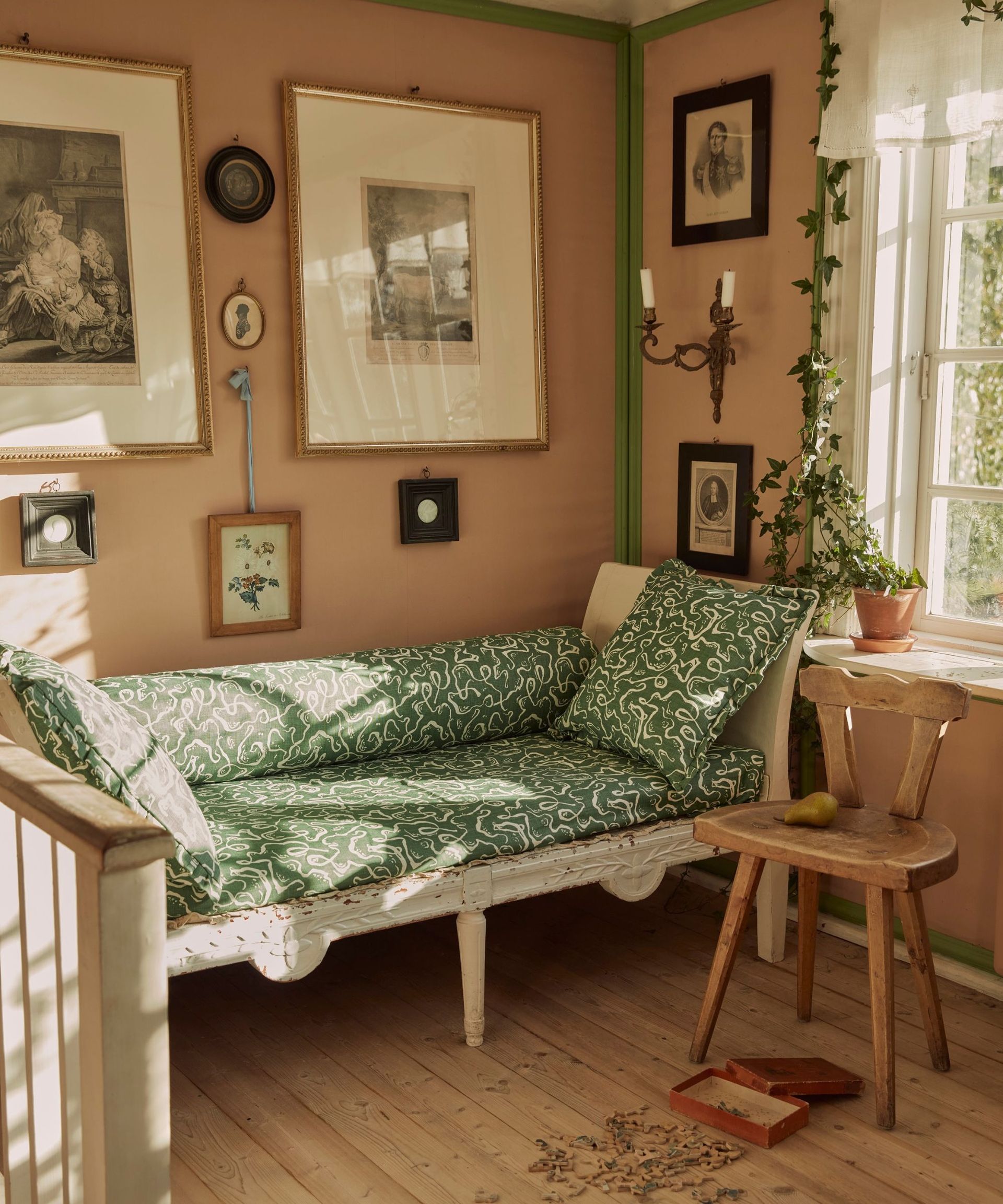 living room with plaster pink walls, green patterned sofa and wooden chair next to window