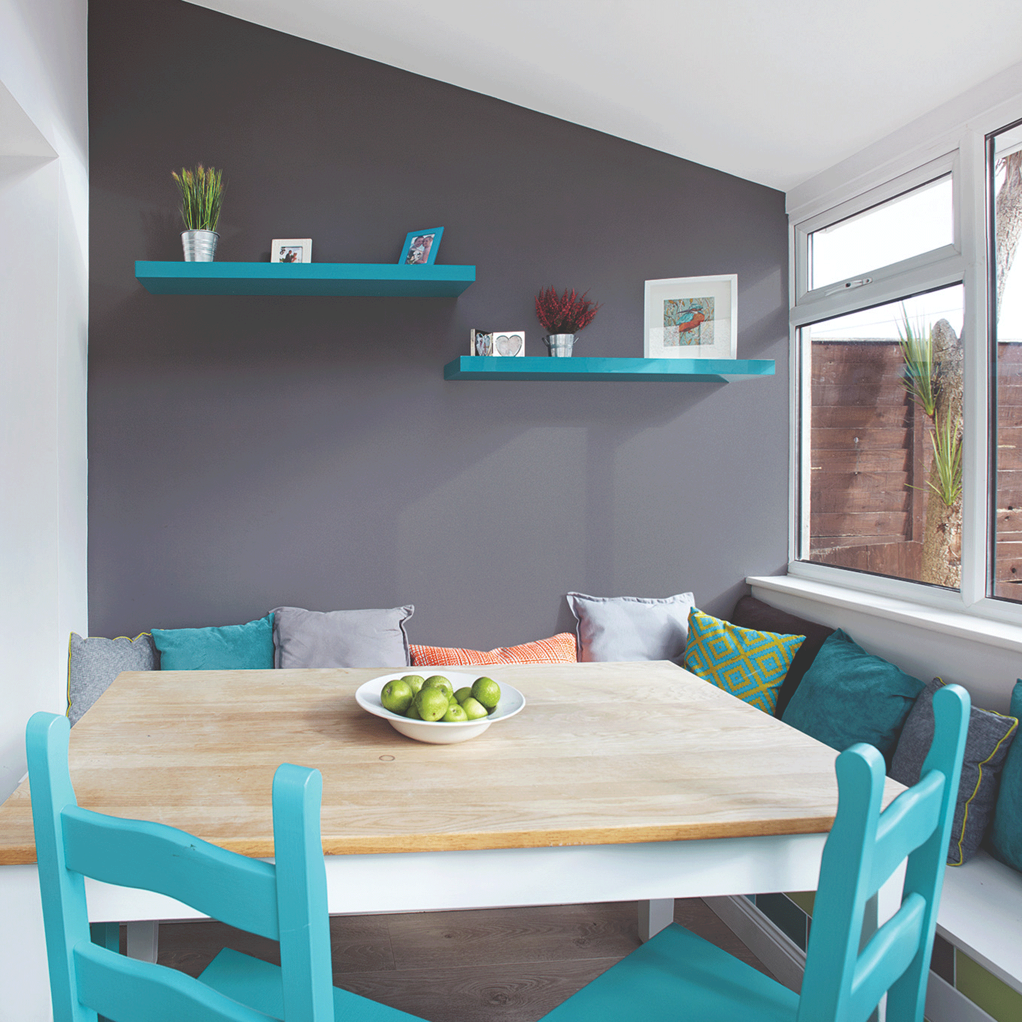 Grey wall with wooden table and turquoise chairs