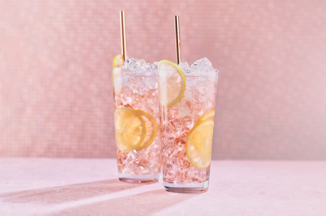Two highball cocktails against a pink backgroundE