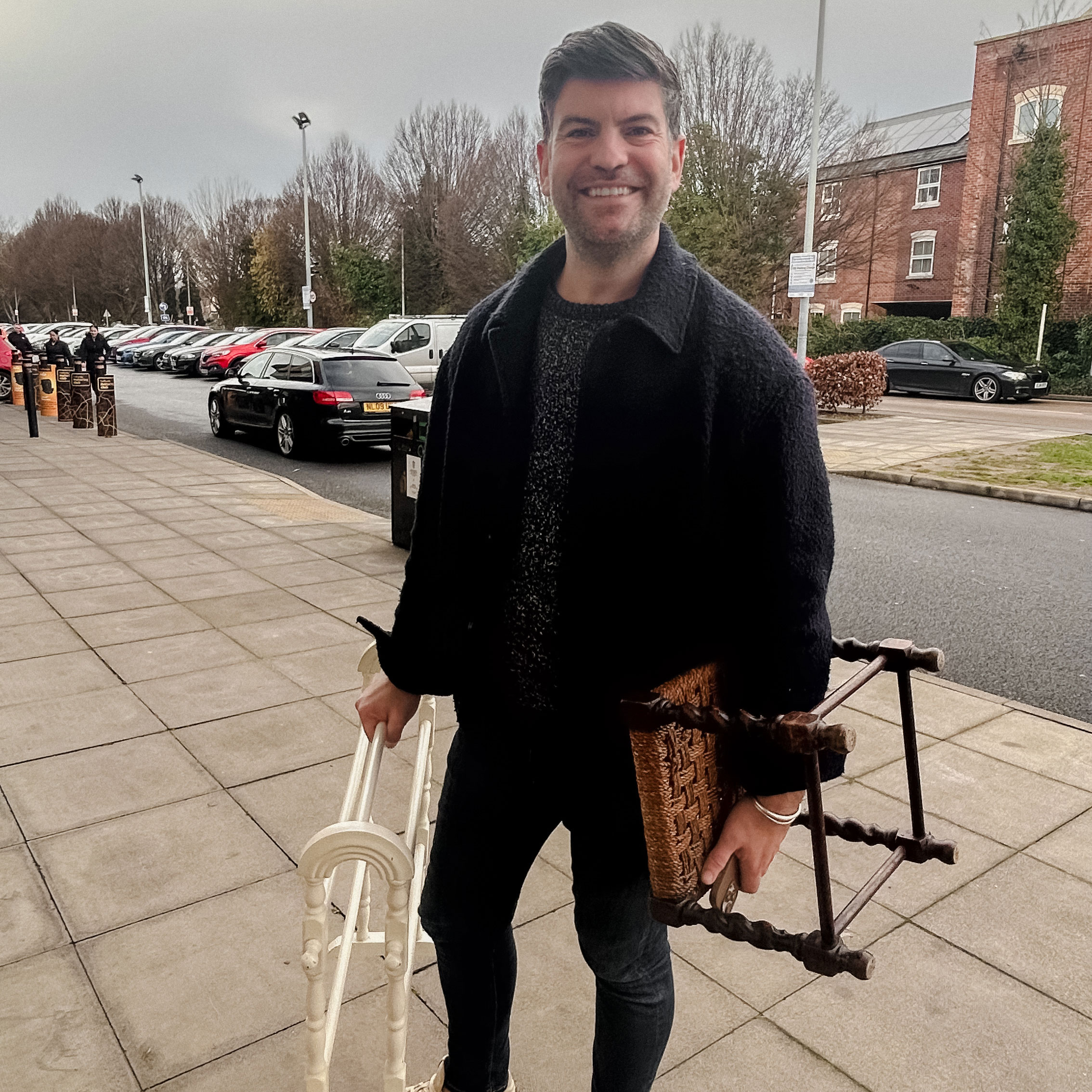 A man standing on the street holding a towel rack and a stool