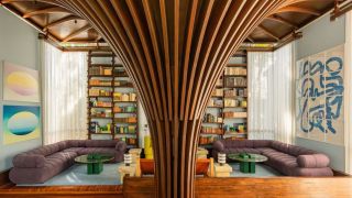 a living room with a purple sofa running its perimeter, a bookcase built into the wall, a timber funnel-shaped column in the center, blue walls, green coffee tables, and sheer curtains