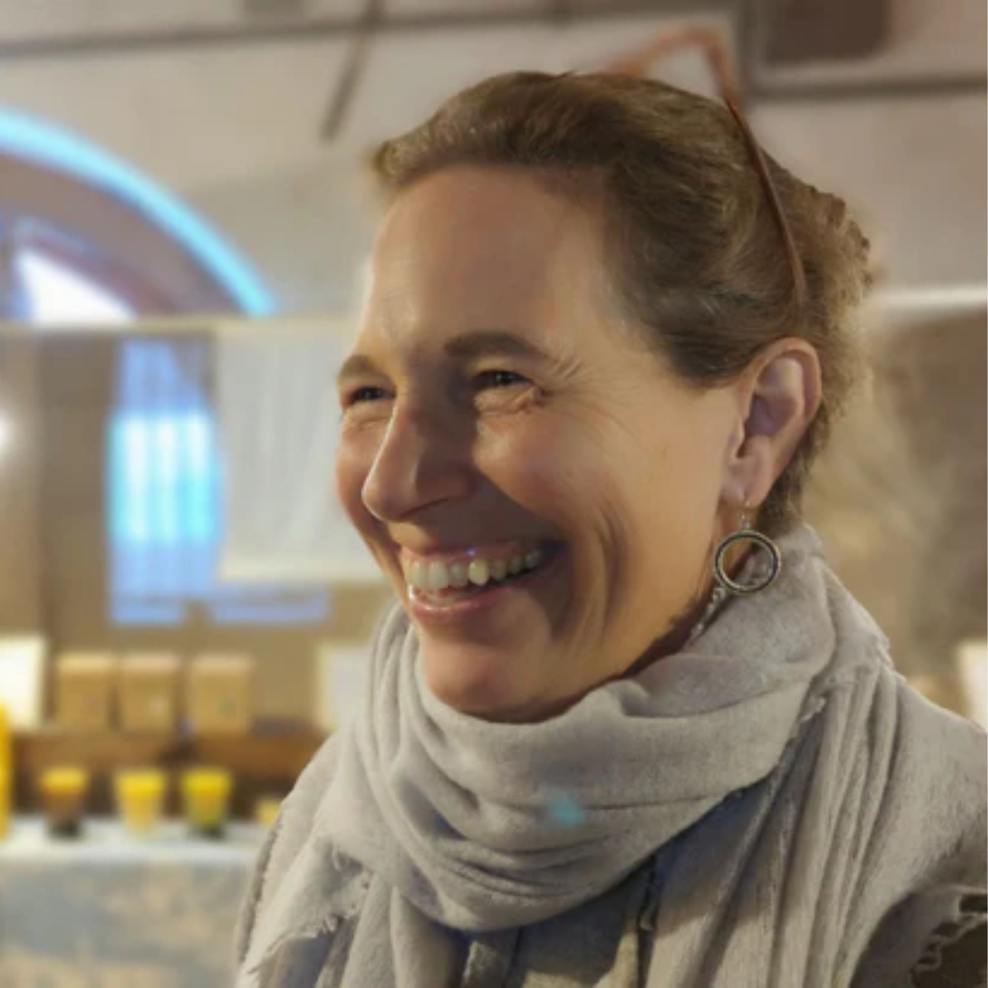A headshot of Amy Keller smiling wearing a grey scarf with her hair up.