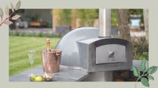 Close up of a stainless steel pizza oven in an outdoor kitchen in a garden with a green background