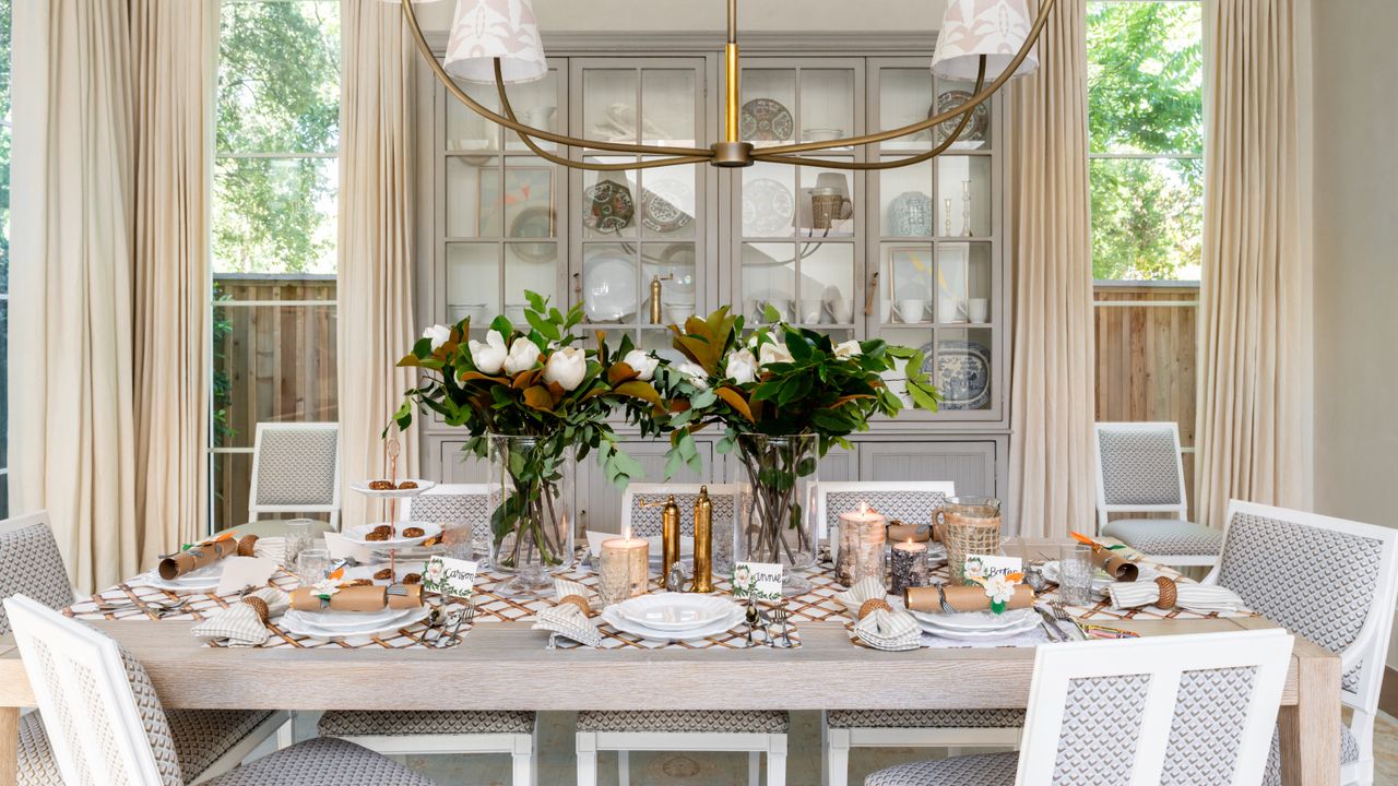 fall dining tablescape with glazed shelving unit behind table, cream drapes, chandelier with fabric shades, flowers, Thanksgiving table, crackers, table settings ideas