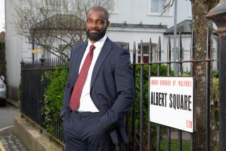 Junior Knight wearing a suit and standing by the Albert Square sign.