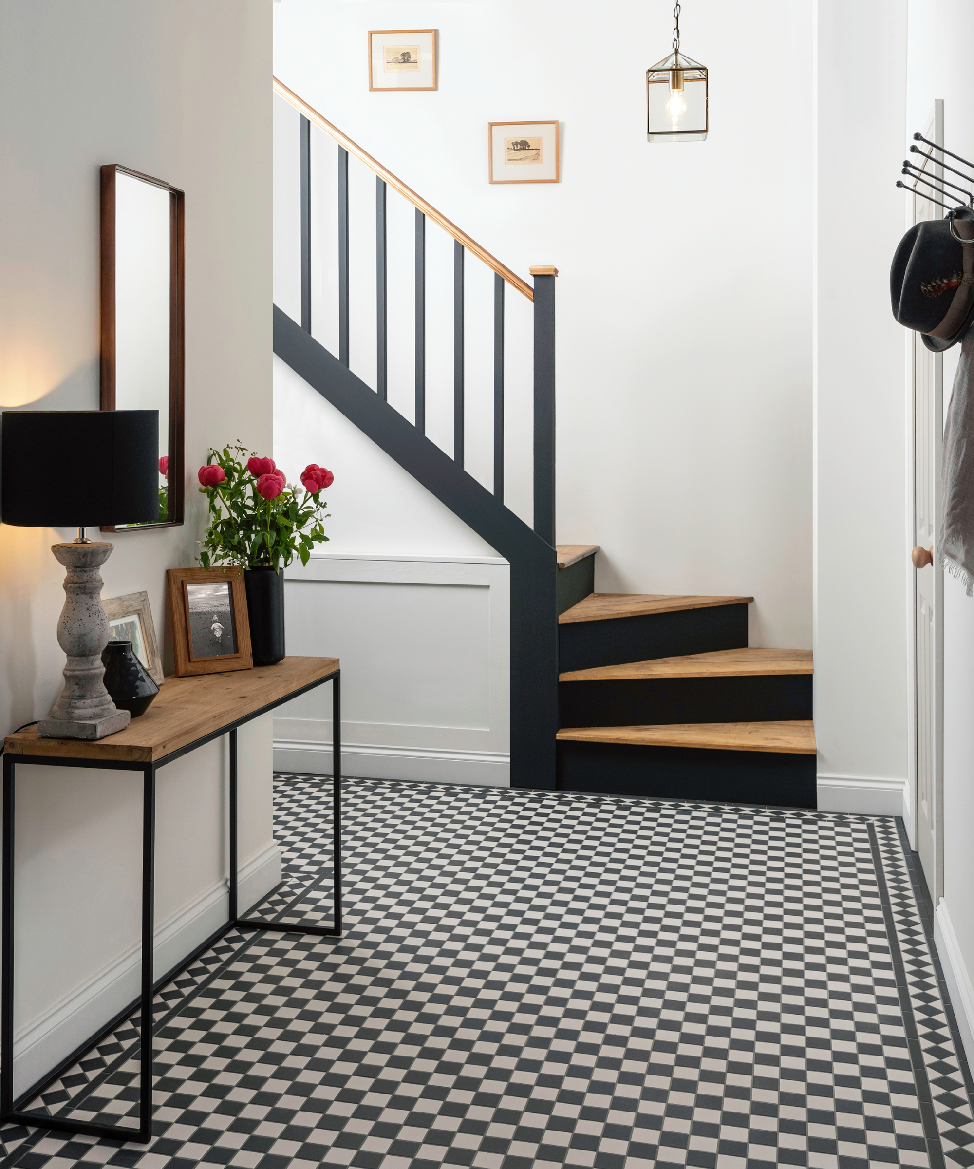 hallway with black and white tiled floor, black and wood staircase, black shaded table lamp and glass and black pendant light