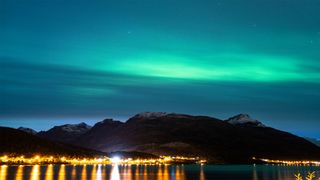 The Northern Lights over a mountain range with bright streetlights in the foreground