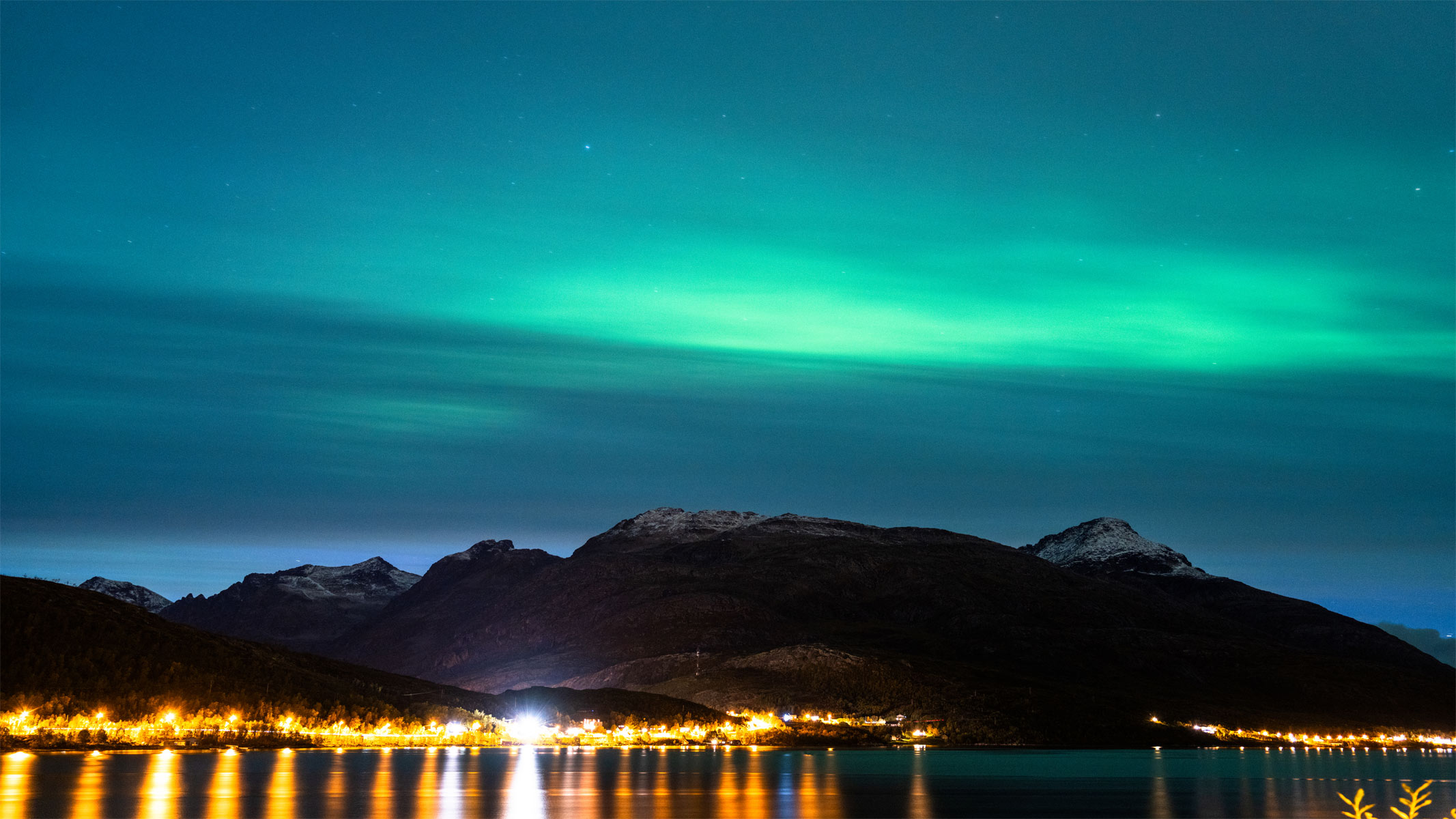 The Northern Lights over a mountain range with bright streetlights in the foreground