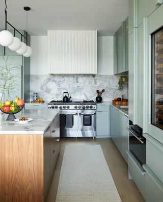 a gray green kitchen with a marble backsplash and reeded cooker hood