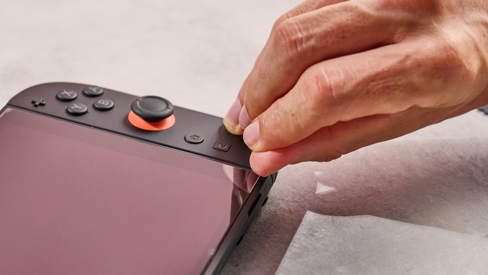 A man applying pressure to the bottom right corner of the Snakebyte Starter Kit S2 screen protector, showing how easily it peels away from the Switch 2 screen.