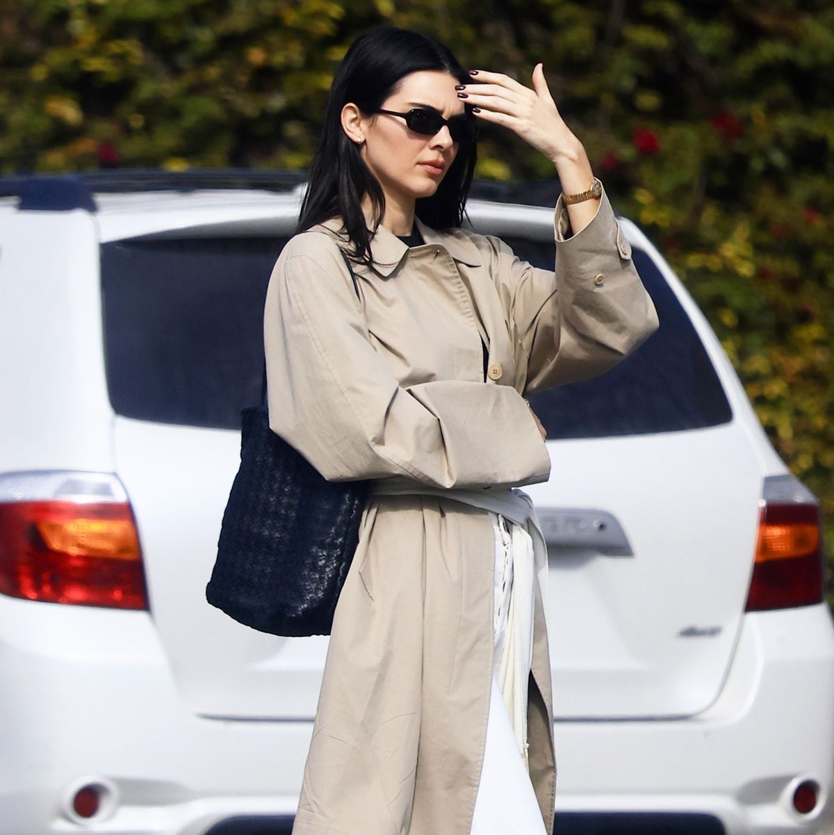 Kendall Jenner wearing a trench coat, scarf belt, white jeans, and black flats