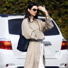 Kendall Jenner wearing a trench coat, scarf belt, white jeans, and black flats