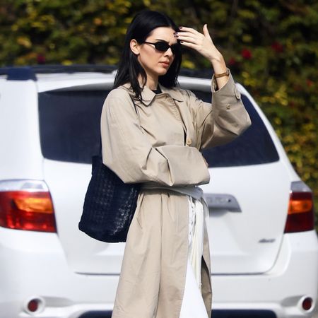 Kendall Jenner wearing a trench coat, scarf belt, white jeans, and black flats