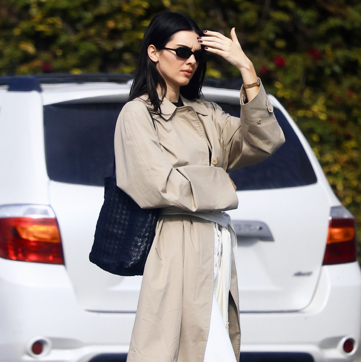 Kendall Jenner wearing a trench coat, scarf belt, white jeans, and black flats