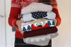 A woman holding a pile of Christmas jumpers