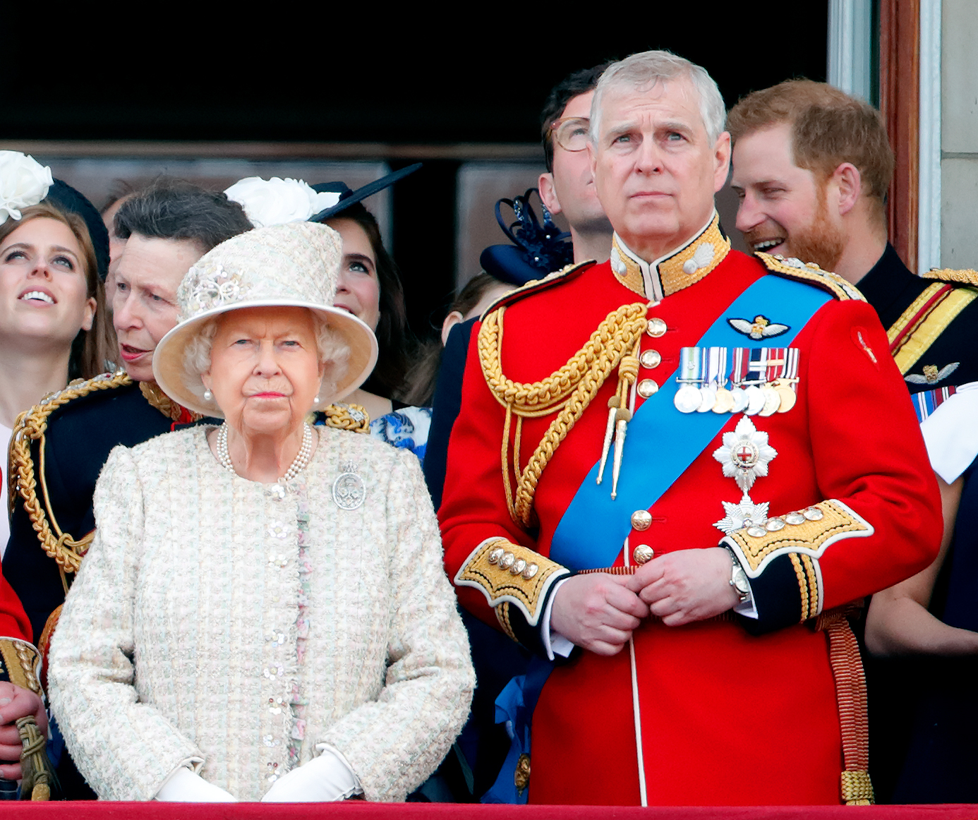 Queen Elizabeth and Prince Andrew standing on the balcony of Buckingham Palace with Prince Harry, Princess Beatrice and Princess Anne visible behind them