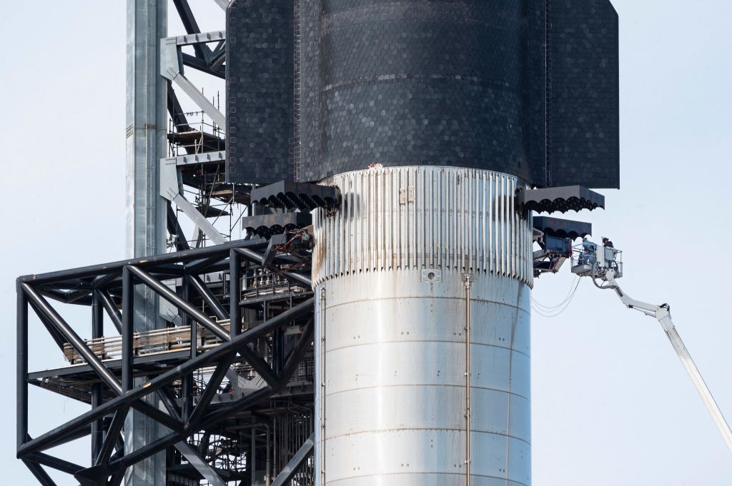 A team inspects the base of SpaceX's first orbital Starship SN20 stacked atop its massive Super Heavy Booster 4 at the company's Starbase facility near Boca Chica Village in South Texas on Feb. 10, 2022