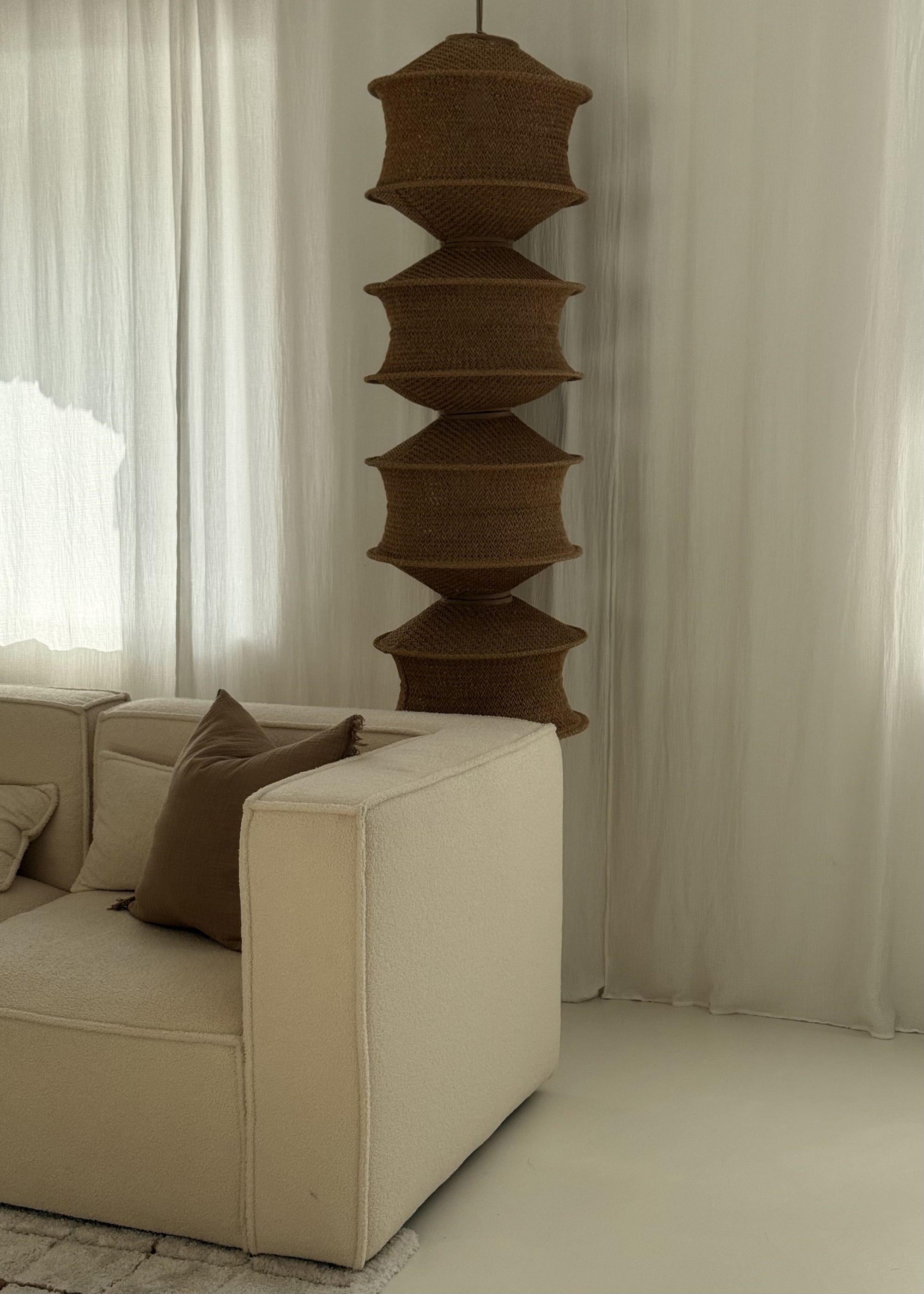 A neutral living room with a cream sofa and a woven pendant lampshade suspended from the ceiling