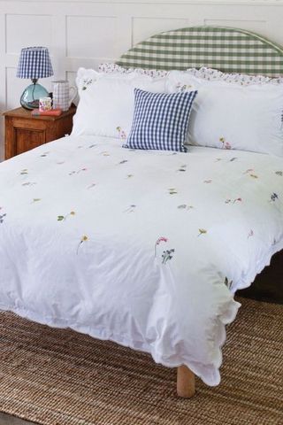 White bedding with embroidered flowers on gingham headboard