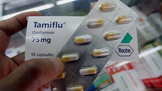 Close-up of a strip of Tamiflu pills being held in front of a box of Tamiflu pills.