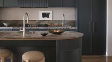 a dark blue kitchen with a curved island and moody brown marble stone counters