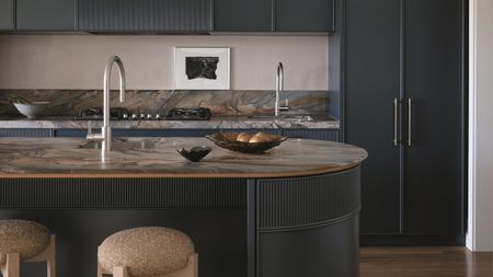 a dark blue kitchen with a curved island and moody brown marble stone counters