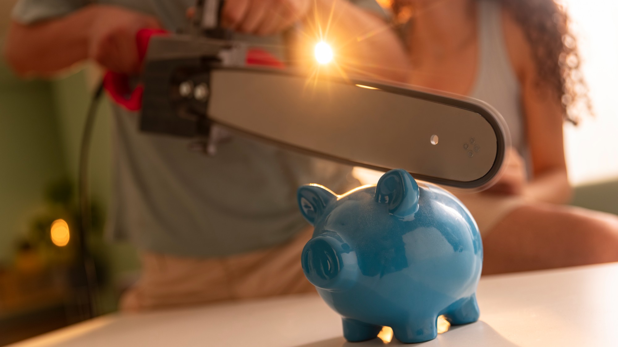 Close-up of young man cutting piggy bank with chainsaw kept on table while woman stands beside him near table.