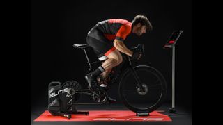 Man on a Wilier road bike fitted to an Elite turbo trainer in a darkened room
