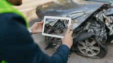 A man uses a tablet to take a picture of a wrecked car.