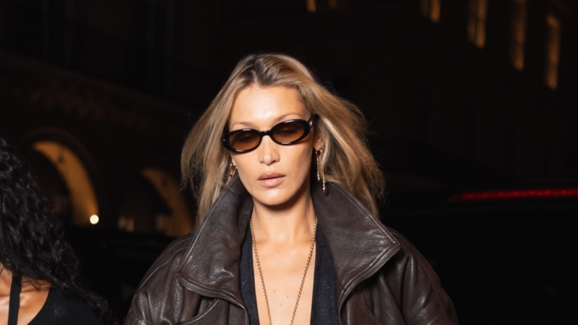 Bella Hadid wearing a brown leather jacket, black capri pants, and pendant necklace
