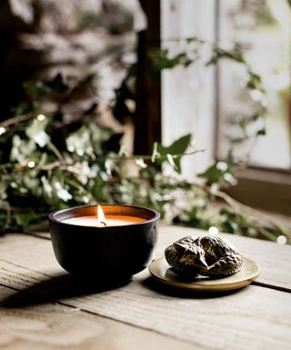 A black candle on a wooden table, with plants in the background